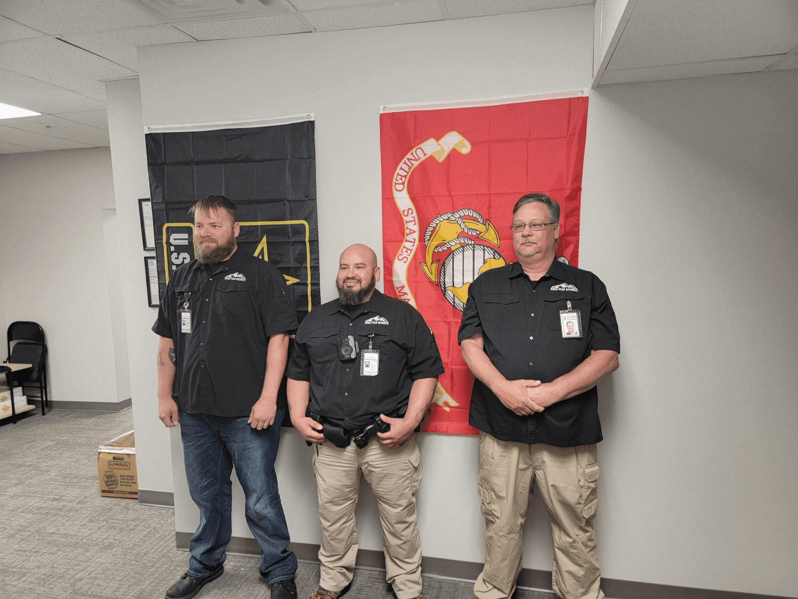 3 security officers standing next to each other in front of a Marine Corps and Military flag