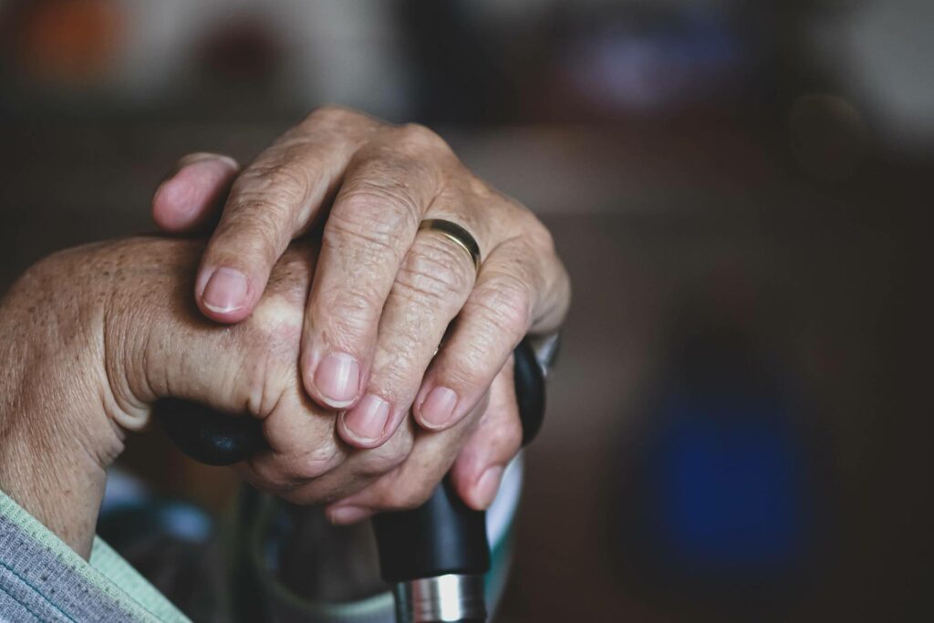 Close up of an older person's hands. They are wearing a wedding band and holding the handle of a cane.