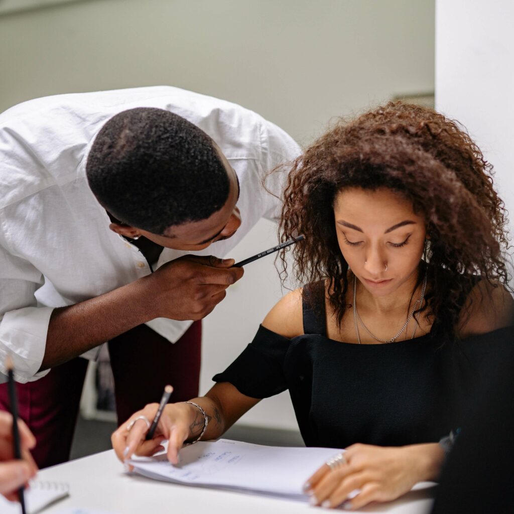 A picture of a man leaning in close to a woman at work while she looks uncomfortable