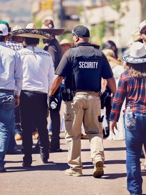 A security officer walks among people in a crowded street scene.
