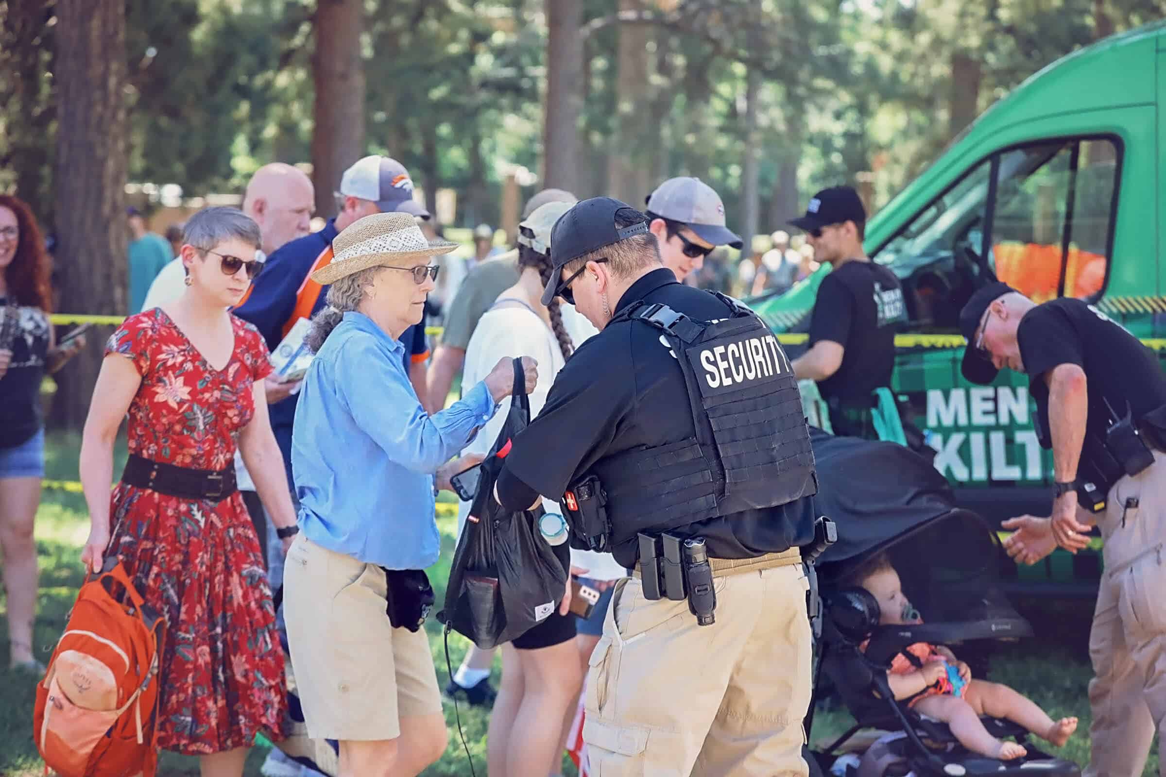 Security personnel inspects bags at an outdoor event.