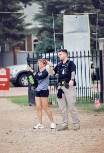 Security officer standing next to an event attendee, both gesturing and giving directions near a gated entrance with parking signs and small American flags nearby.