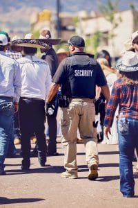 Security officer walking through a crowd during a cultural event, surrounded by people wearing cowboy hats and traditional attire.