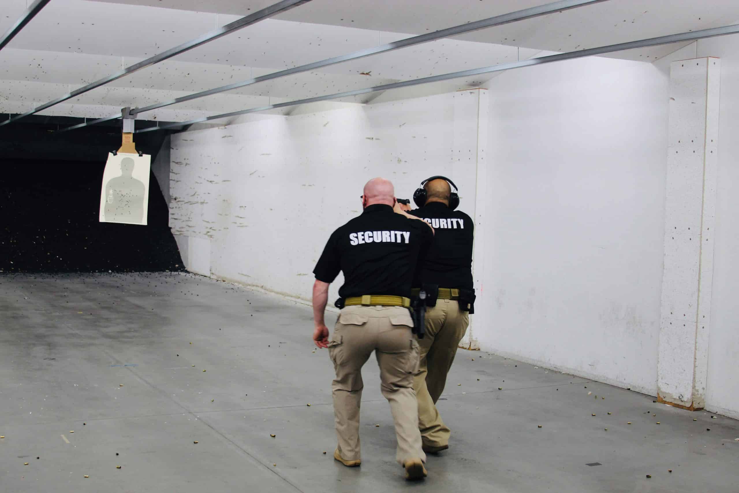 Two security personnel at a shooting range with a silhouette target.