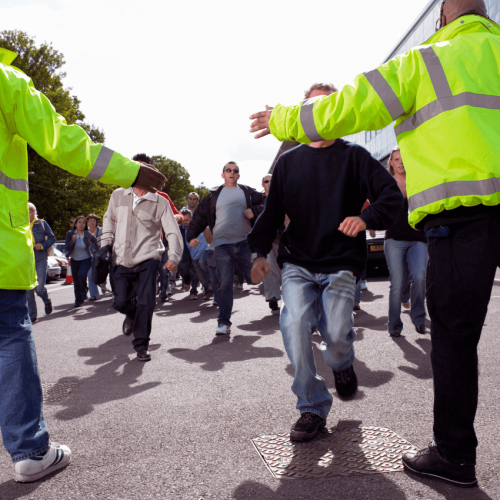 The picture shows two security guards in yellow jackets keeping a large crowd from entering an event.
